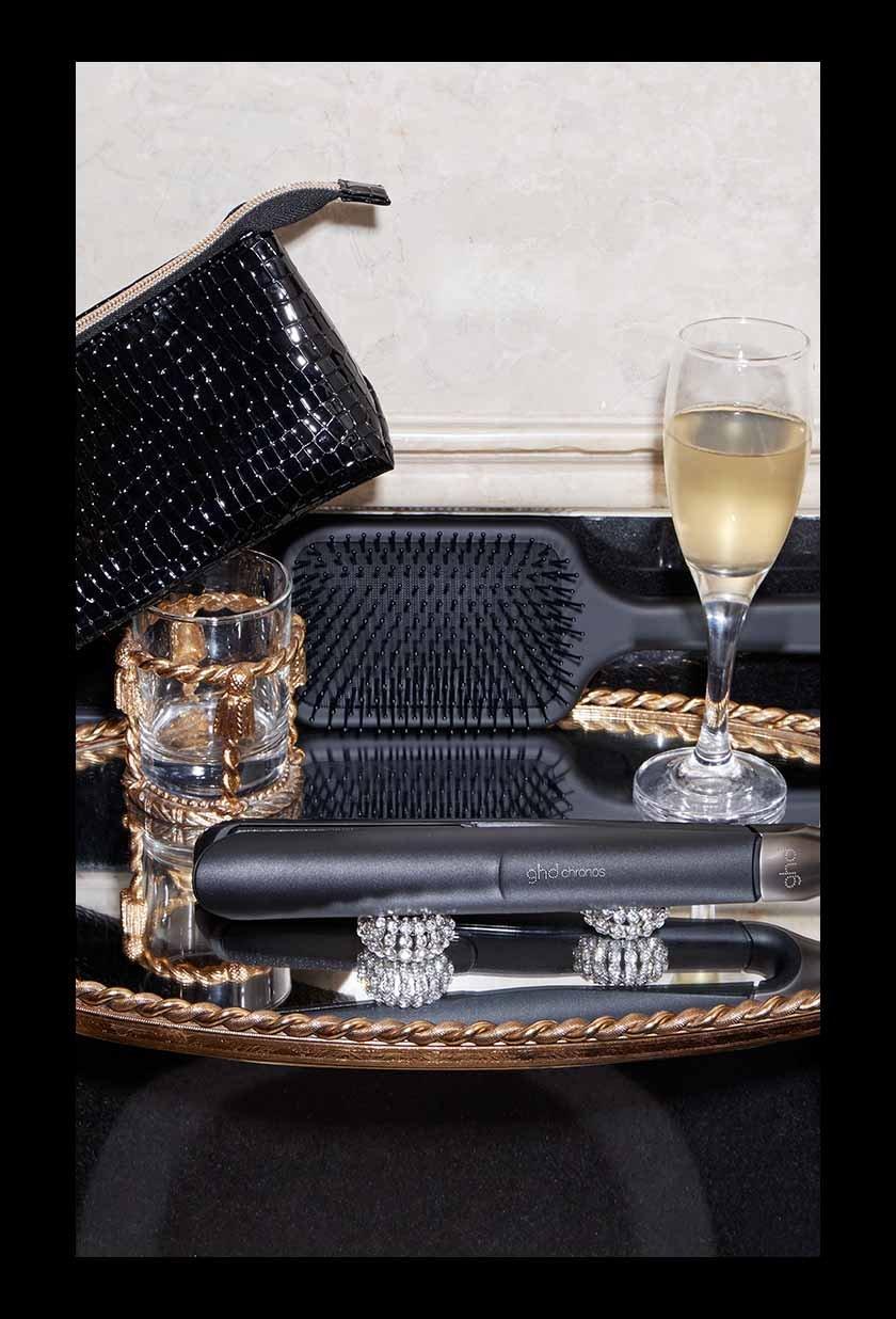 ghd chronos Haarstyler auf einem Silbertablett mit Accessoires und Sektglas